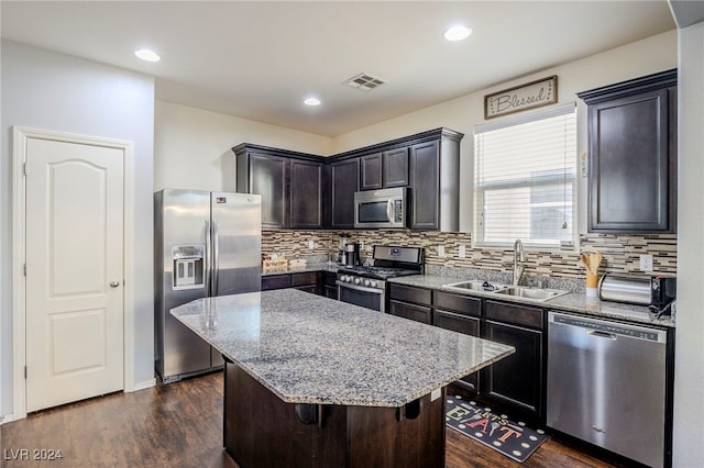 kitchen with dark hardwood / wood-style flooring, light stone counters, stainless steel appliances, sink, and a center island