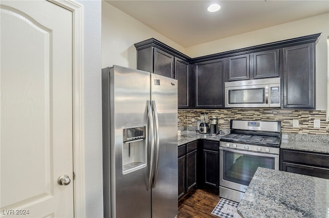 kitchen featuring appliances with stainless steel finishes, backsplash, light stone counters, and dark wood-type flooring