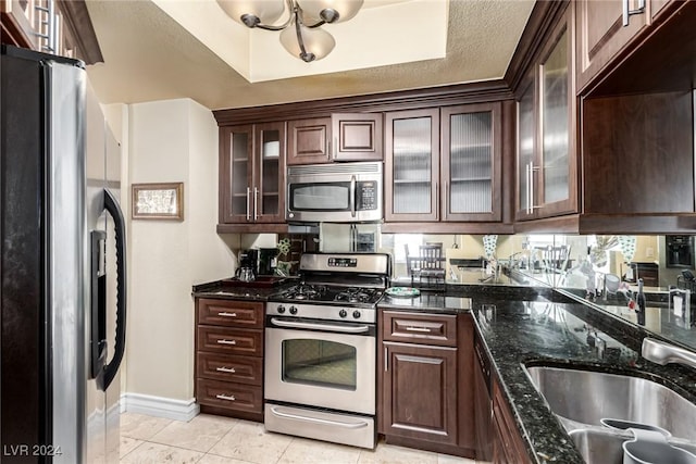 kitchen featuring appliances with stainless steel finishes, dark stone counters, a textured ceiling, dark brown cabinetry, and sink