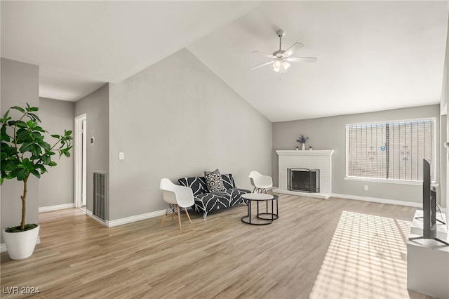 sitting room with ceiling fan, light wood-type flooring, high vaulted ceiling, and a brick fireplace