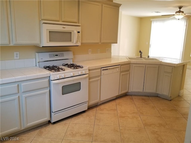 kitchen featuring white appliances, sink, light tile patterned floors, tile counters, and kitchen peninsula