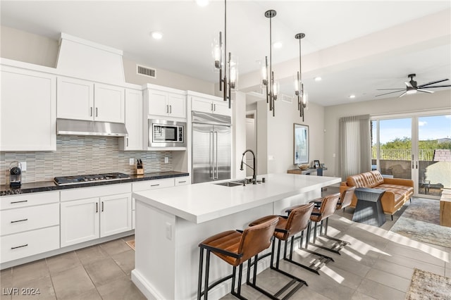 kitchen with sink, built in appliances, ceiling fan, an island with sink, and decorative light fixtures