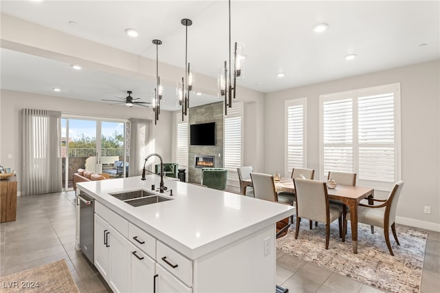 kitchen featuring a large fireplace, sink, pendant lighting, a center island with sink, and white cabinets