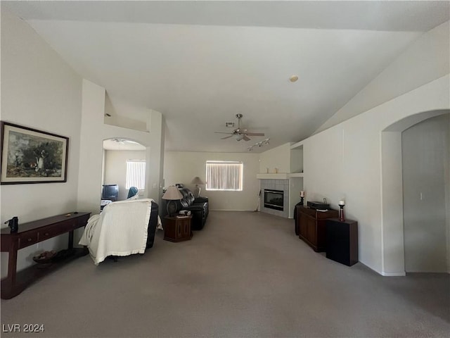 living room featuring carpet flooring, ceiling fan, vaulted ceiling, and a tiled fireplace