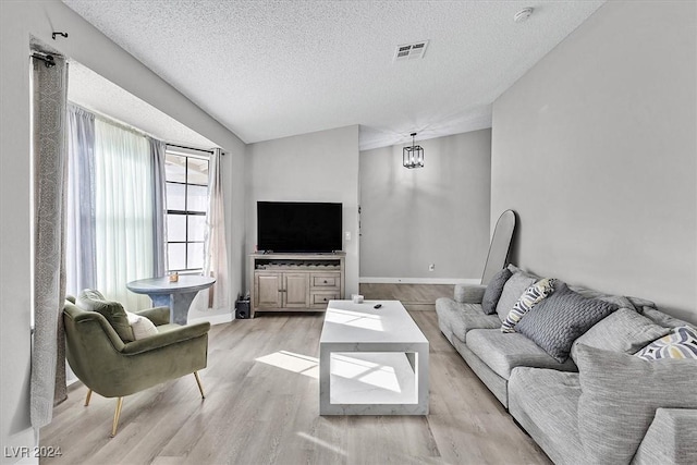 living room with light hardwood / wood-style floors, an inviting chandelier, a textured ceiling, and vaulted ceiling