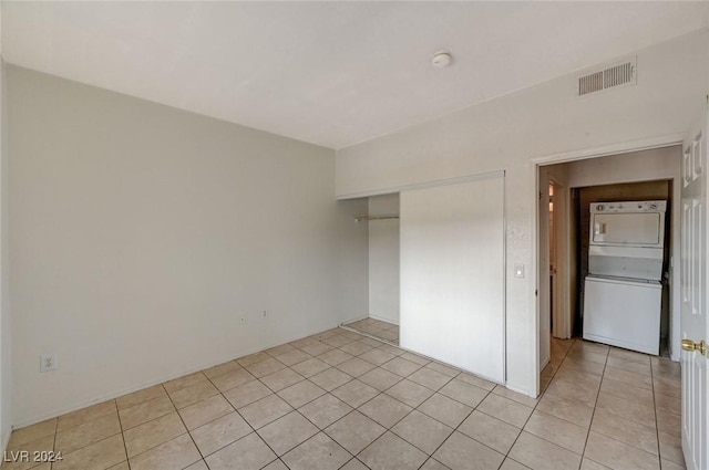 unfurnished bedroom featuring light tile patterned floors, a closet, and stacked washer and clothes dryer