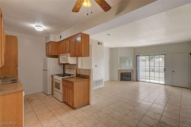 kitchen with a tiled fireplace, ceiling fan, light tile patterned flooring, and white appliances