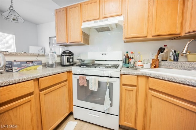 kitchen with sink, light brown cabinets, light hardwood / wood-style flooring, hanging light fixtures, and white gas stove