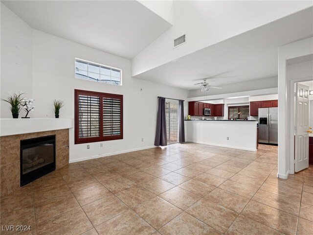 unfurnished living room with a fireplace, light tile patterned floors, high vaulted ceiling, and ceiling fan