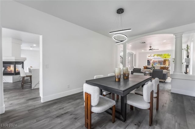 dining area featuring a multi sided fireplace, dark hardwood / wood-style flooring, ornate columns, and ceiling fan