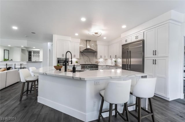 kitchen with high end appliances, a kitchen breakfast bar, wall chimney range hood, a large island, and white cabinetry