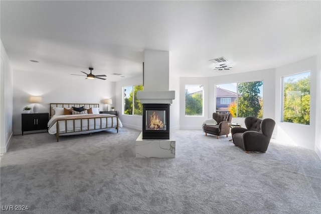 carpeted bedroom featuring a multi sided fireplace and ceiling fan