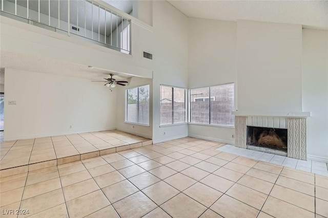 unfurnished living room with ceiling fan, light tile patterned flooring, a towering ceiling, and a fireplace