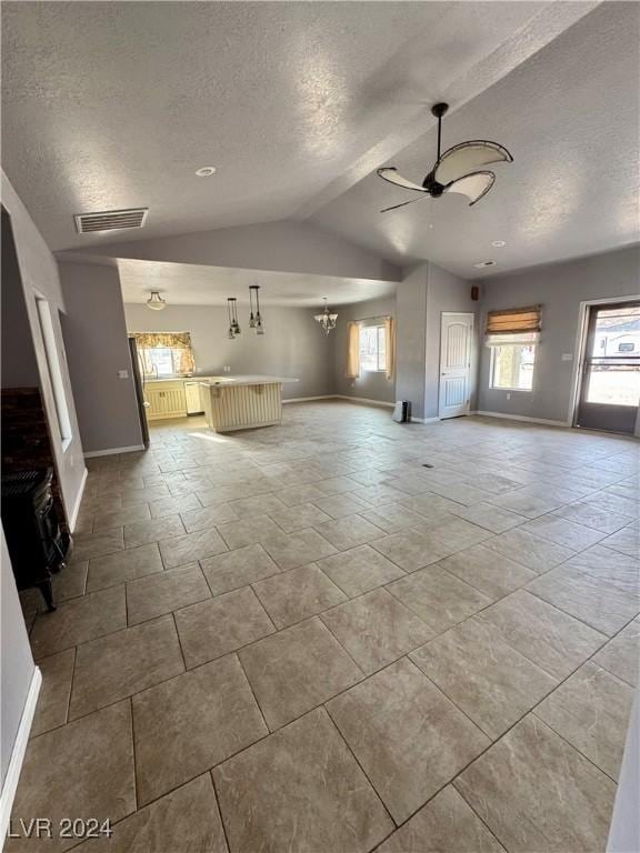 unfurnished living room featuring a textured ceiling, ceiling fan with notable chandelier, vaulted ceiling, and a wealth of natural light