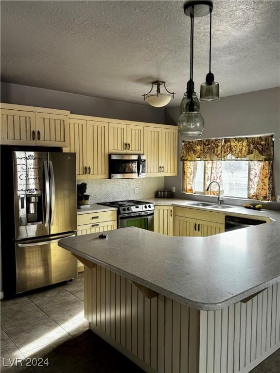 kitchen with sink, tile patterned flooring, a textured ceiling, appliances with stainless steel finishes, and decorative light fixtures