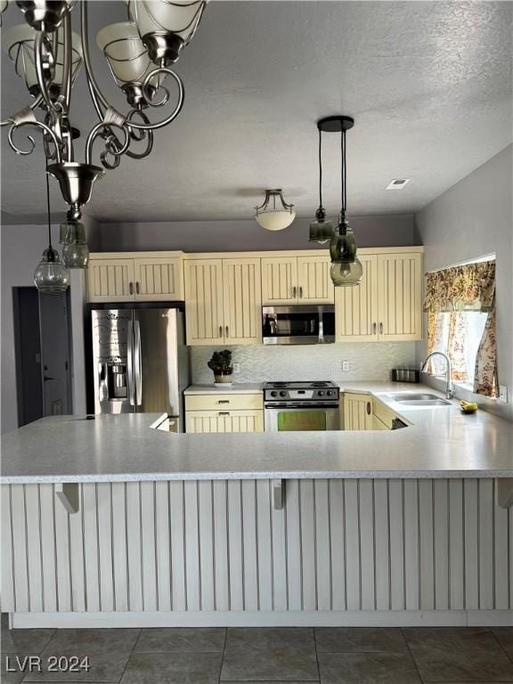 kitchen with sink, stainless steel appliances, kitchen peninsula, cream cabinets, and a chandelier