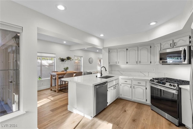 kitchen featuring sink, light wood-type flooring, kitchen peninsula, stainless steel appliances, and white cabinets