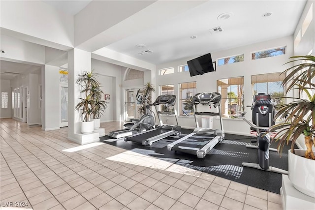 exercise room featuring light tile patterned flooring and a towering ceiling