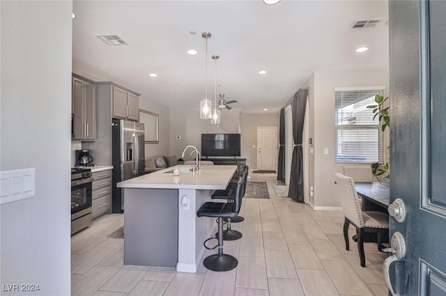 kitchen featuring a breakfast bar, stainless steel appliances, a kitchen island with sink, sink, and gray cabinets