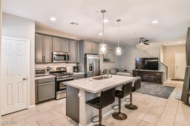 kitchen with ceiling fan, decorative light fixtures, a kitchen bar, a kitchen island with sink, and appliances with stainless steel finishes