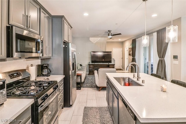 kitchen with appliances with stainless steel finishes, ceiling fan, a kitchen island with sink, sink, and hanging light fixtures