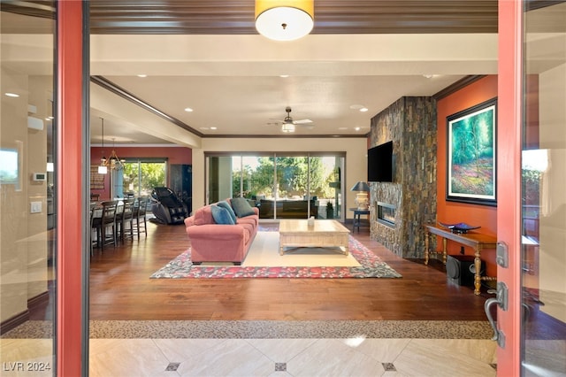 living room featuring a fireplace, light wood-type flooring, ceiling fan, and crown molding