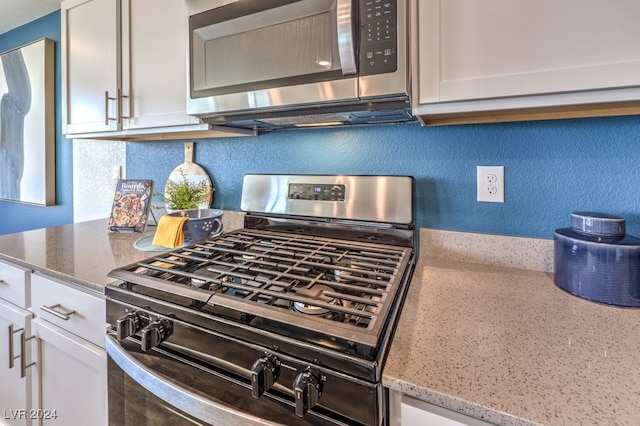 room details with backsplash, white cabinetry, light stone counters, and appliances with stainless steel finishes