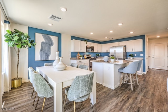 kitchen with a kitchen bar, appliances with stainless steel finishes, a center island, dark hardwood / wood-style floors, and white cabinetry