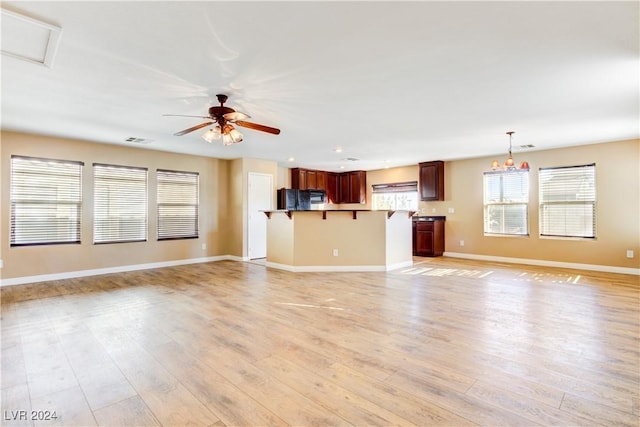 unfurnished living room with ceiling fan with notable chandelier and light hardwood / wood-style flooring