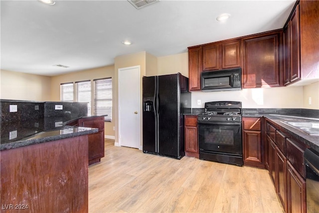 kitchen with dark stone counters, sink, black appliances, and light hardwood / wood-style floors