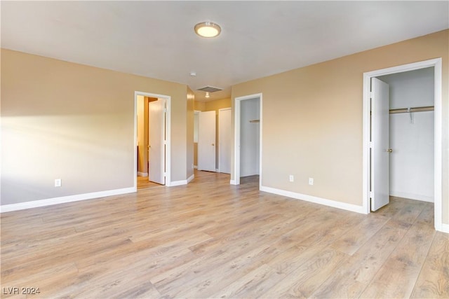 unfurnished bedroom featuring a walk in closet, ensuite bathroom, light hardwood / wood-style flooring, and a closet