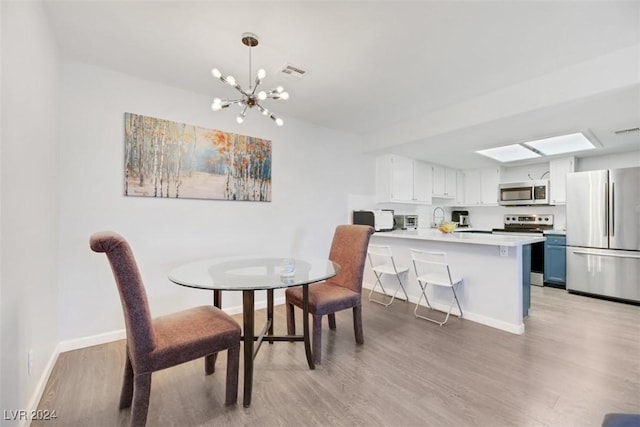 dining area featuring sink, light hardwood / wood-style floors, and an inviting chandelier