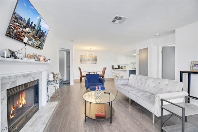 living room with a chandelier, light wood-type flooring, and a tiled fireplace