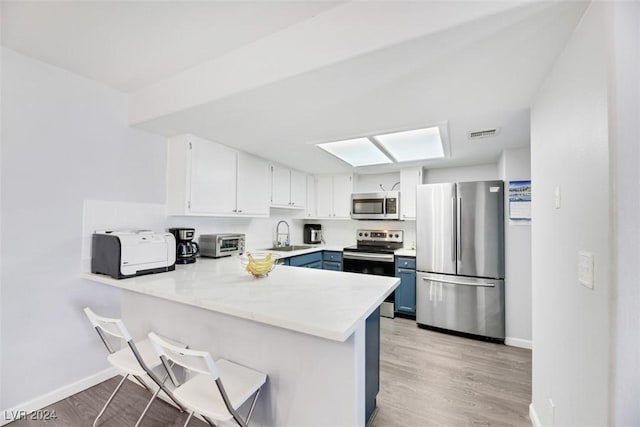 kitchen with blue cabinets, kitchen peninsula, light wood-type flooring, appliances with stainless steel finishes, and white cabinetry