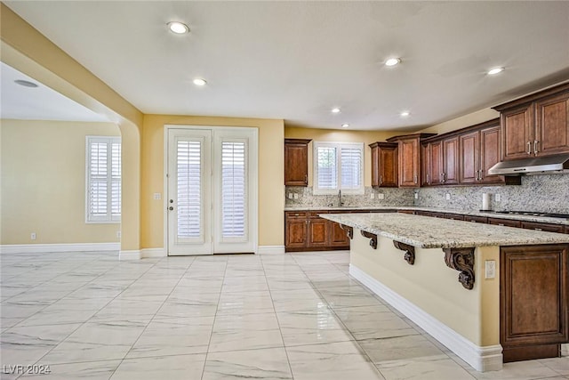 kitchen with a kitchen bar, light stone countertops, backsplash, sink, and a center island