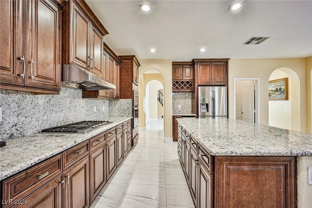 kitchen with a center island, stainless steel appliances, light stone counters, and tasteful backsplash