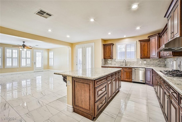 kitchen featuring decorative backsplash, light stone counters, stainless steel appliances, ceiling fan, and a center island