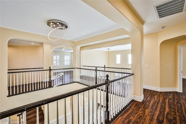 corridor with dark hardwood / wood-style floors, an inviting chandelier, and plenty of natural light