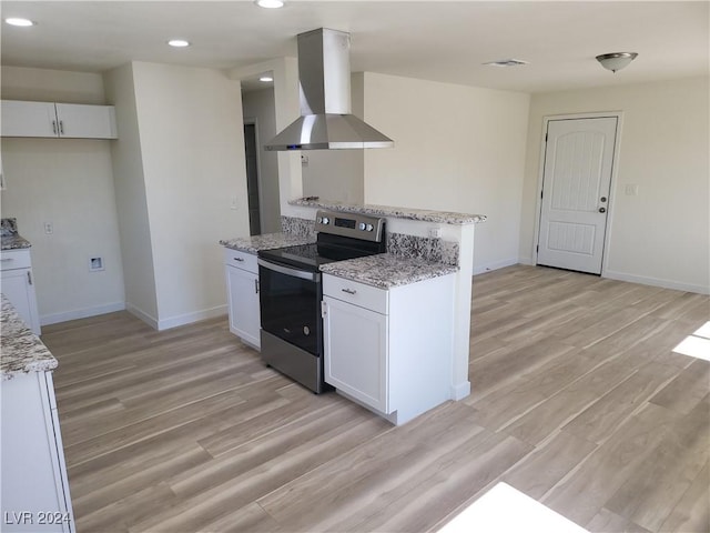 kitchen with light stone countertops, wall chimney exhaust hood, stainless steel electric stove, white cabinets, and light hardwood / wood-style floors