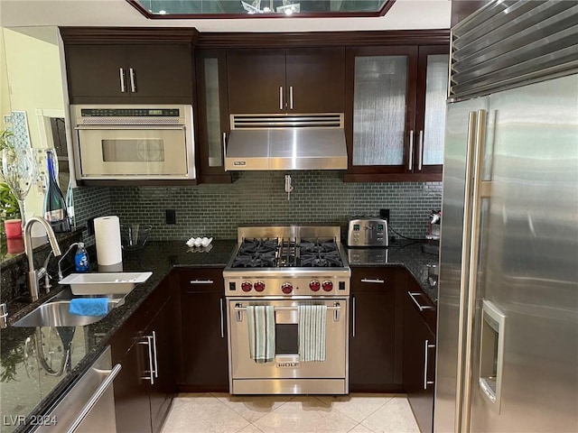 kitchen featuring dark stone counters, dark brown cabinetry, sink, exhaust hood, and high quality appliances