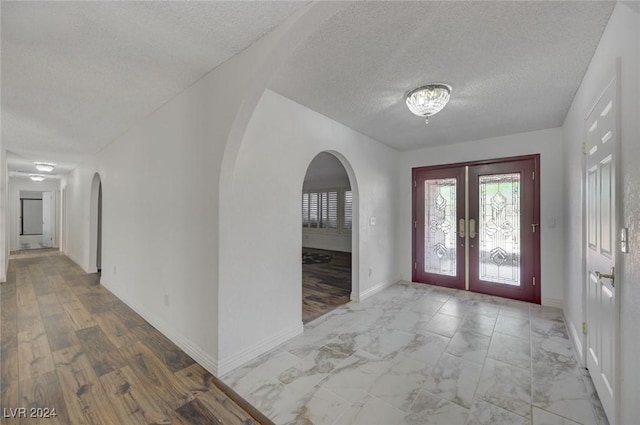 entryway with light hardwood / wood-style floors, a textured ceiling, and french doors