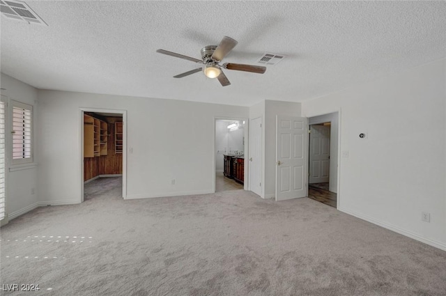 unfurnished bedroom featuring ensuite bathroom, ceiling fan, a spacious closet, a textured ceiling, and light colored carpet