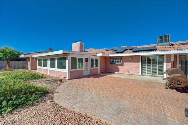 back of property with a sunroom, a patio, and solar panels