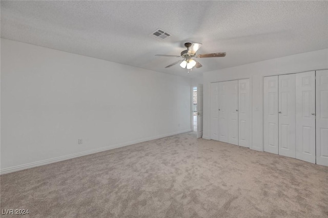 unfurnished bedroom featuring ceiling fan, light colored carpet, a textured ceiling, and multiple closets