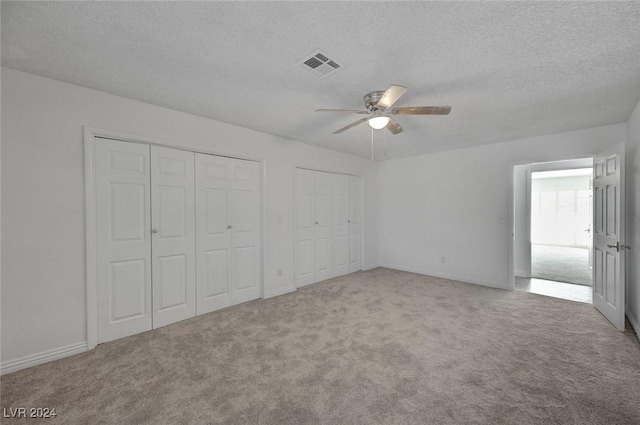 unfurnished bedroom with a textured ceiling, ceiling fan, carpet floors, and two closets