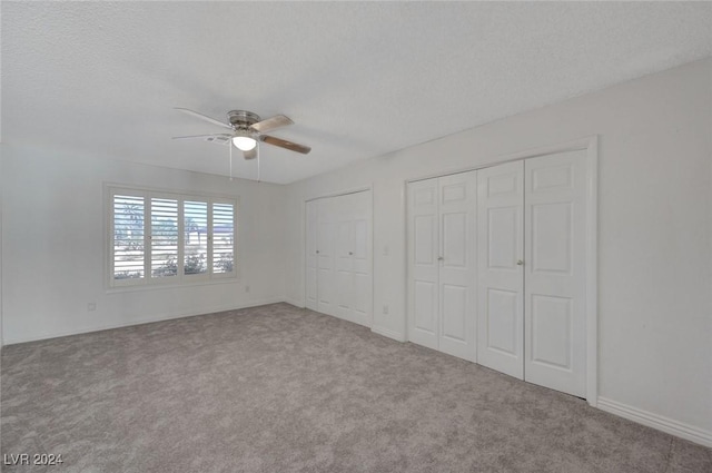 unfurnished bedroom featuring ceiling fan, carpet floors, a textured ceiling, and multiple closets