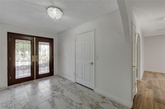 entrance foyer with french doors, a textured ceiling, and light hardwood / wood-style flooring