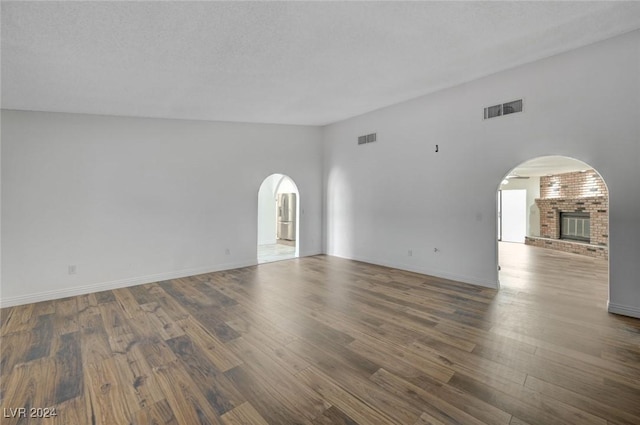 empty room with a fireplace, a high ceiling, a textured ceiling, and dark hardwood / wood-style floors