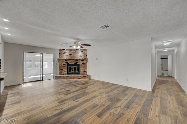 unfurnished living room featuring a textured ceiling, light wood-type flooring, and a brick fireplace