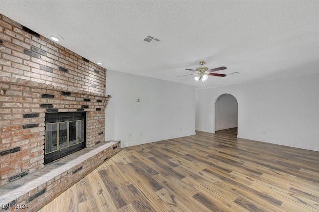 unfurnished living room featuring hardwood / wood-style floors, a textured ceiling, a brick fireplace, and ceiling fan